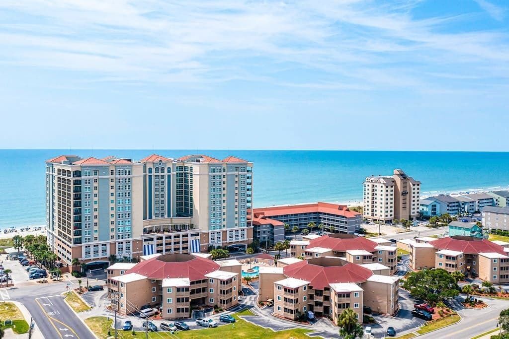 A coastal hotel complex with multiple buildings, a parking area, and a view of the ocean.