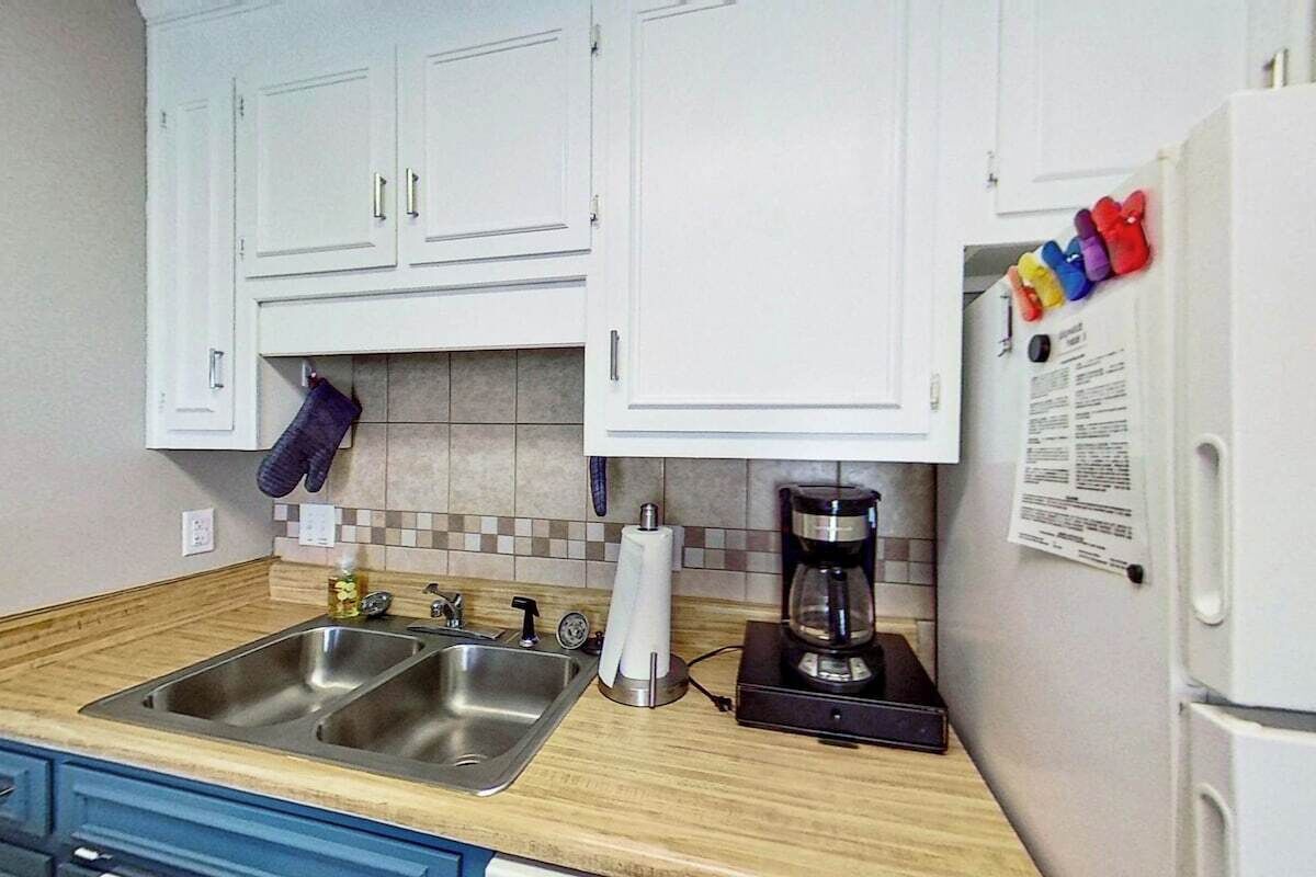 A kitchen with white cabinets, a double sink, a coffee maker, and a refrigerator with magnets.