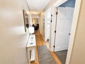 A hallway with a white door, a small table with a lamp, and a rug leading to a room. - Shipwatch Pointe II L-302 (Myrtle Beach)