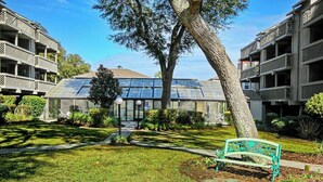 Ein Gebäude mit einem Glaswintergarten, umgeben von einer gepflegten Rasenfläche und einer Bank.