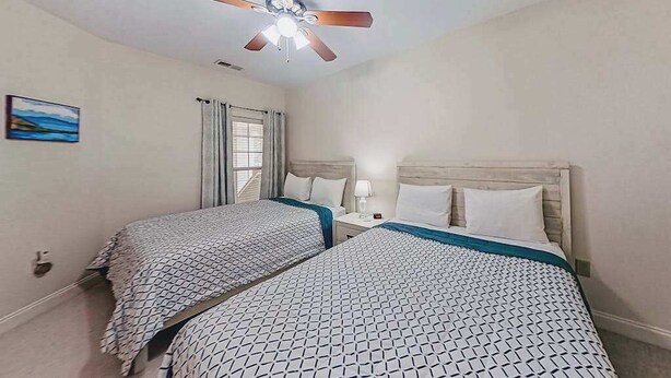 A hotel room with two beds, a ceiling fan, a nightstand with a lamp, and a painting on the wall. - 1033 World Tour Unit 306 (Myrtle Beach)