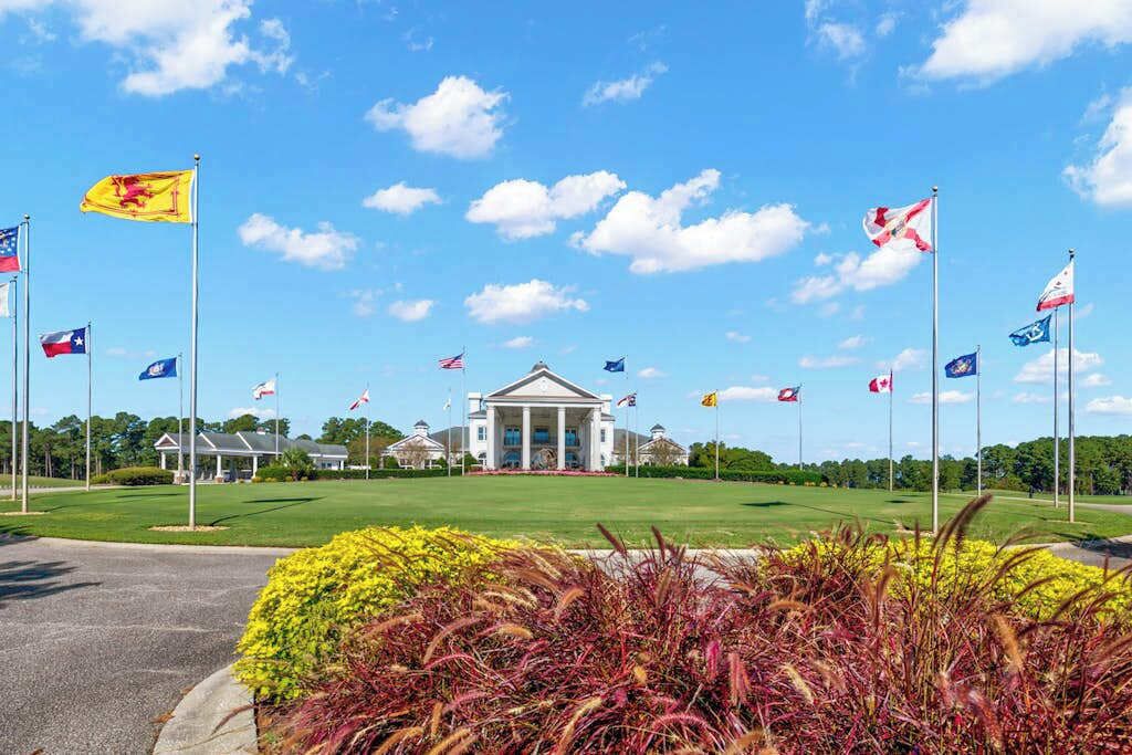 A building with a central entrance, surrounded by a lawn with various flags, and a clear sky.