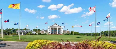 A building with a central entrance, surrounded by a lawn with various flags, and a clear sky.