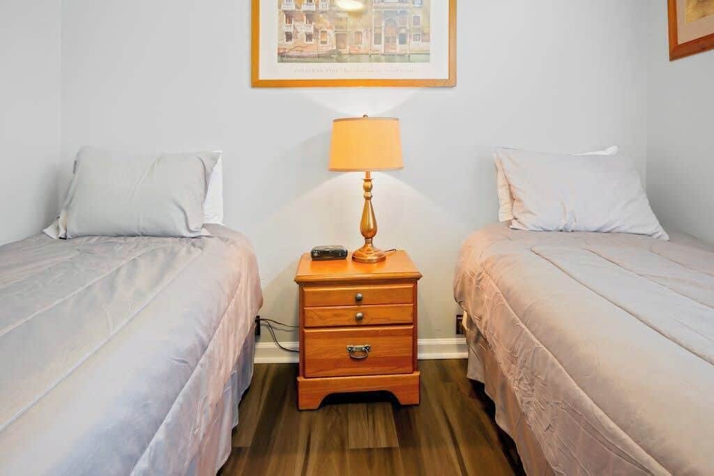 A room with two beds, a nightstand with a lamp, and a framed picture on the wall.