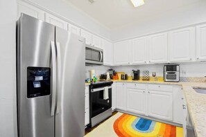 A modern kitchen with white cabinets, stainless steel appliances, and a colorful rug. - Village at the Glens L-205 (Little River)