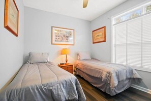 A bedroom with two beds, a nightstand with a lamp, and framed pictures on the wall. - Village at the Glens L-205 (Little River)