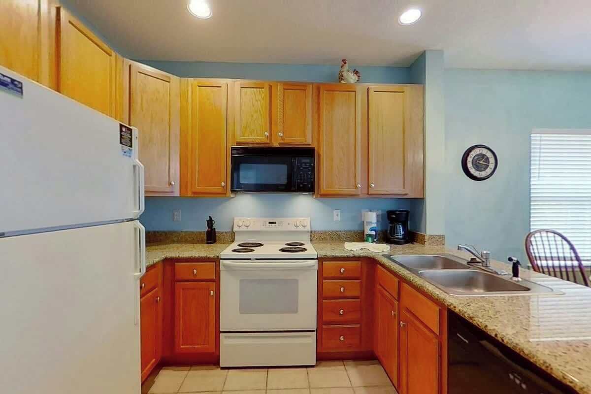 A kitchen with wooden cabinets, a white stove, a microwave, and a sink.