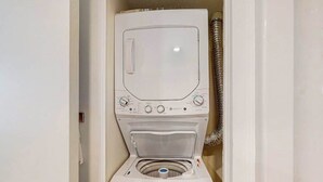 Une machine à laver compacte, conçue pour être fixée au mur, dotée d’une porte à chargement frontal, d’un panneau de commande et d’un tuyau pour le raccordement à l’eau.