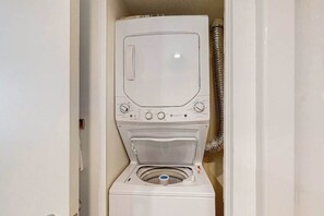 Máquina de lavar compacta, fixada na parede, com abertura frontal, painel de controle e mangueira para ligação à água.