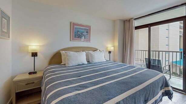 Une chambre d’hôtel avec un lit, des tables de chevet, un tableau et un balcon avec vue.