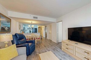 A living room with a sofa, a television, and a dining area with chairs and a table. - Z-Beach Colony Unit 415 (Myrtle Beach)