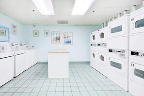 A laundry facility with multiple washing machines, a central counter, and framed pictures on the wall. - Z-Beach Colony Unit 415 (Myrtle Beach)