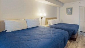 Une chambre d’hôtel avec deux lits, une table de chevet, une lampe fixée au mur et un tableau encadré.