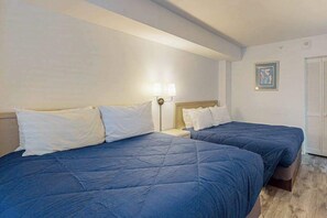 Quarto de hotel com duas camas, uma mesa de cabeceira, uma luminária fixada na parede e um quadro emoldurado.