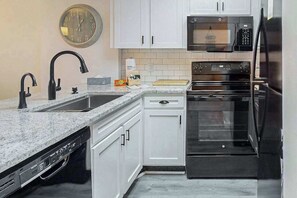 Uma cozinha com armários brancos, micro-ondas preto, forno de aço inoxidável e lava-louças.
