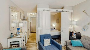Um espaço de estar compacto com escrivaninha, uma poltrona azul, sofá, cama e guarda-roupa.