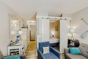 A compact living space with a desk, a blue armchair, a sofa, a bed, and a wardrobe. - The Sand Shack - Litchfield Inn 251 (Pawleys Island)