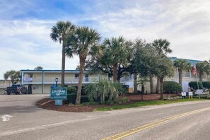 A hotel with a registration sign, palm trees, and a building with a blue roof. - The Sand Shack - Litchfield Inn 251 (Pawleys Island)