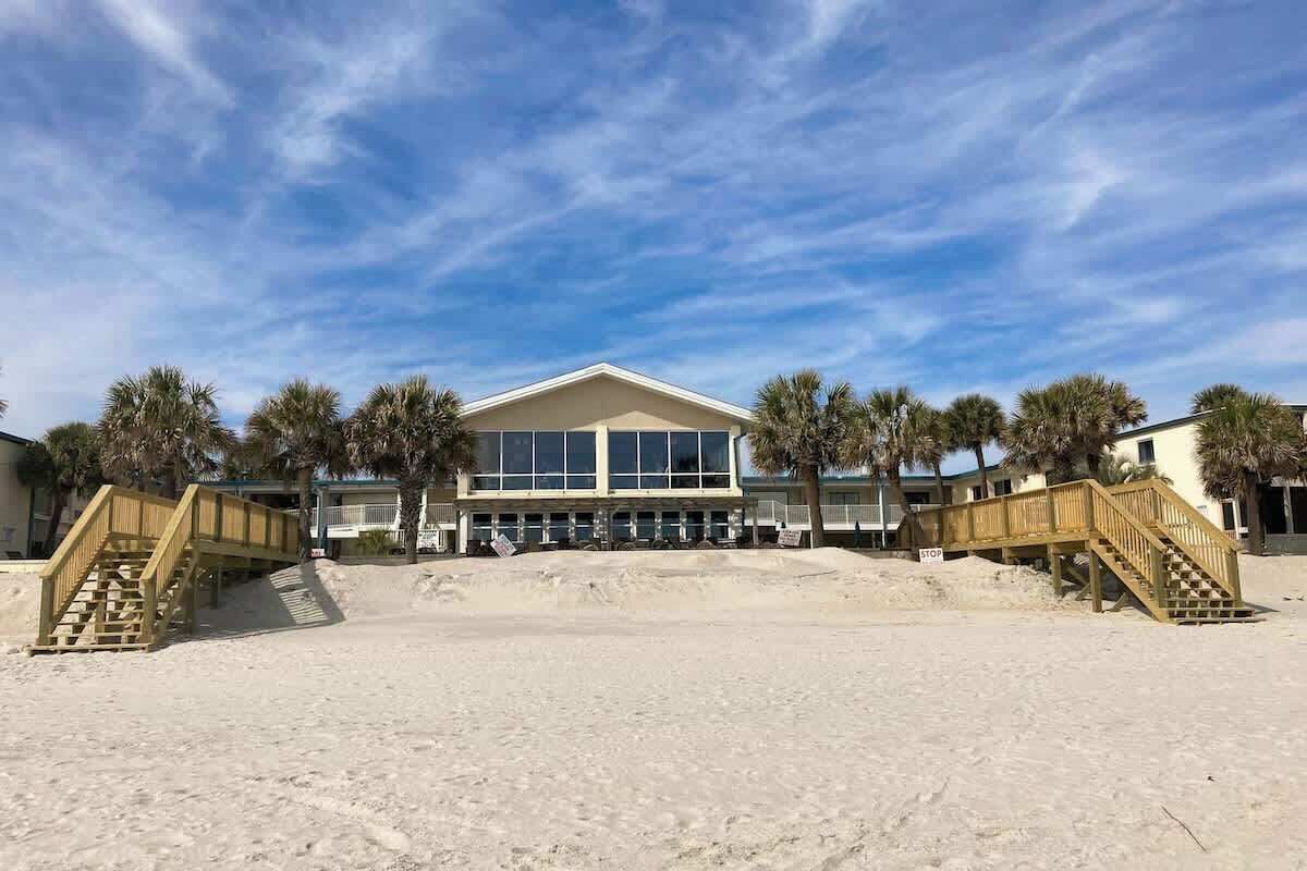Un hôtel situé en bord de mer, avec un grand bâtiment, des passerelles en bois et des palmiers.