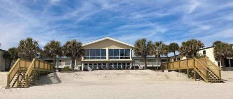 Un hôtel situé en bord de mer, avec un grand bâtiment, des passerelles en bois et des palmiers.