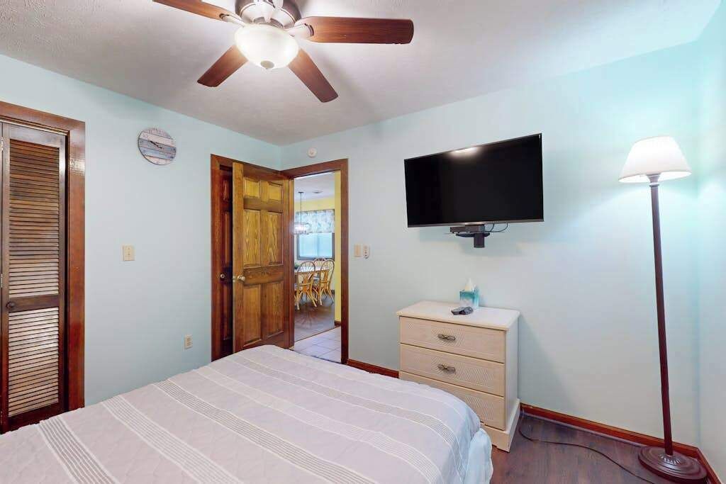 Ein Schlafzimmer mit einem Bett, einem Deckenventilator, einem Fernseher, einer Kommode und einer Lampe.