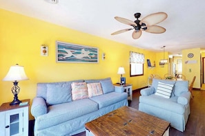 A living room with a sofa, armchair, and coffee table, a ceiling fan, and artwork on the walls. - Shipwatch Pointe II Q-305 (Myrtle Beach)