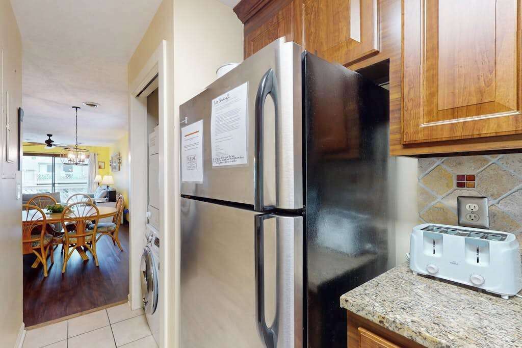 A kitchen with a stainless steel refrigerator, a toaster, wooden cabinets, and a dining area with a table and chairs.