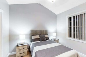 A bedroom with a bed, bedside tables, a window with blinds, and a ceiling light. - Riverwalk Unit 301 Condo (Myrtle Beach)