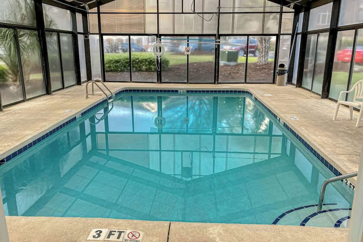 An indoor swimming pool with a 3 ft depth marker, surrounded by glass walls with a view of the outdoors.