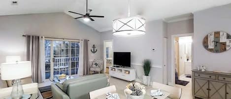 A modern living room with a sofa, television, dining table, and chairs.