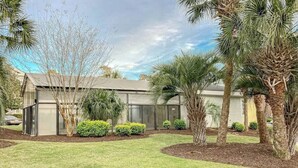 A modern building with a flat roof, surrounded by a well-maintained lawn and various trees. - Riverwalk Unit 301 Condo (Myrtle Beach)