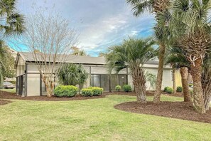 A modern building with a flat roof, surrounded by a well-maintained lawn and various trees. - Riverwalk Unit 301 Condo (Myrtle Beach)