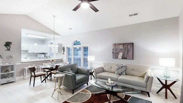 A modern living room with a sofa, armchairs, a coffee table, and a dining area with chairs and a table. - Riverwalk Unit 301 Condo (Myrtle Beach)