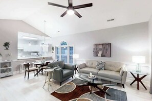 A modern living room with a sofa, armchairs, a coffee table, and a dining area with chairs and a table. - Riverwalk Unit 301 Condo (Myrtle Beach)