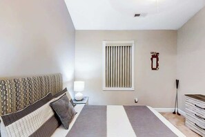 A bedroom with a bed, bedside table, lamp, window, and a dresser. - Riverwalk Unit 301 Condo (Myrtle Beach)