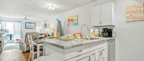 A kitchen with white cabinets, a marble countertop, and a coffee maker.