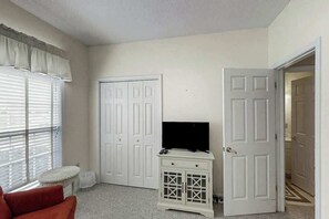 A room with a television on a cabinet, a red chair, and a closet with white doors. - Scotch Broom Unit E-104 (Little River)