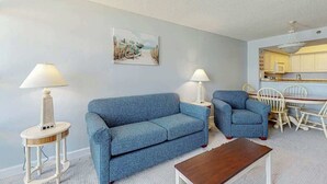 Uma sala de estar com sofá, duas poltronas, uma mesa de centro e um canto de jantar com mesa e cadeiras.