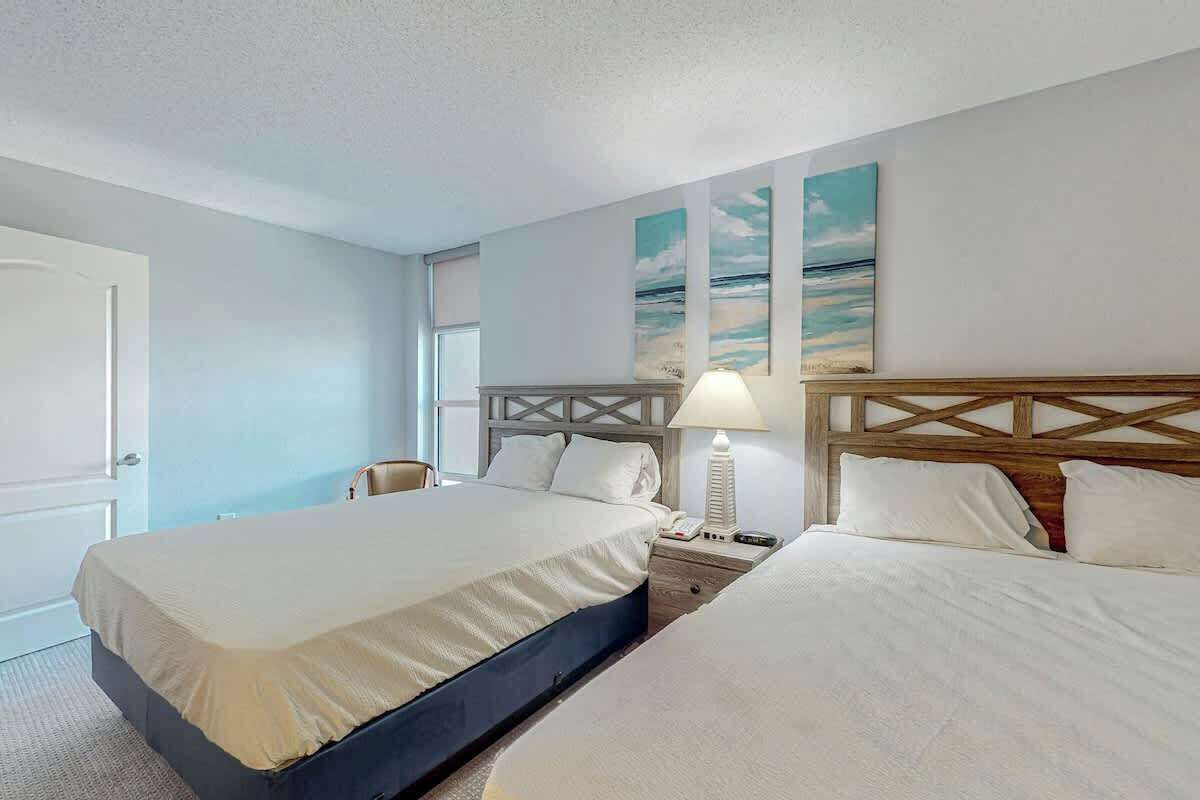 A hotel room with a large bed, bedside tables, a lamp, and artwork on the wall.
