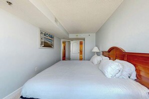 A hotel room with a large bed, a wooden headboard, a bedside lamp, and a door leading to another room. - Carolinian Beach Resort 0730 (Myrtle Beach)