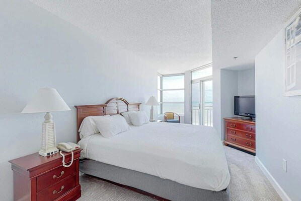 A hotel room with a large bed, a TV, a dresser, and a window with a view. - Carolinian Beach Resort 0730 (Myrtle Beach)