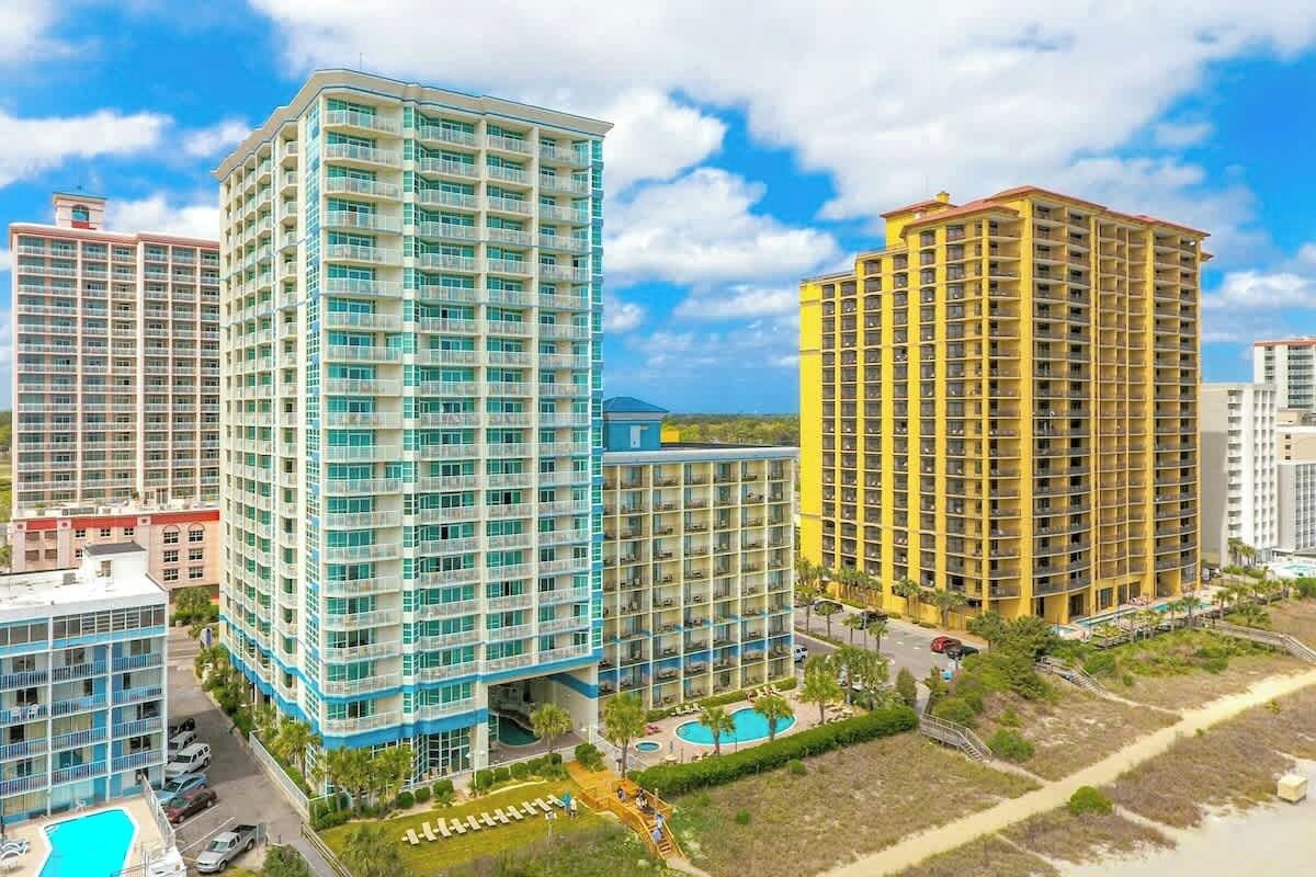 A high-rise hotel with multiple floors, a swimming pool, and a beach area.