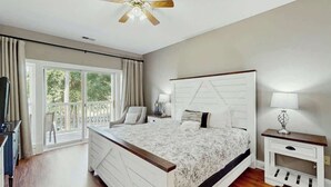 A bedroom with a bed, bedside tables, a ceiling fan, and a window with curtains. - Cypress Point Retreat 202 (Myrtle Beach)
