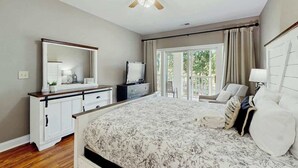 A bedroom with a large bed, a dresser, a mirror, a ceiling fan, and a view of the outdoors through a sliding door. - Cypress Point Retreat 202 (Myrtle Beach)