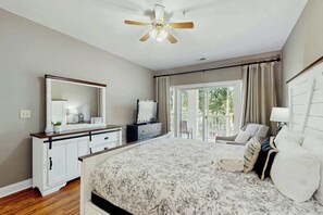 A bedroom with a large bed, a dresser, a mirror, a ceiling fan, and a view of the outdoors through a sliding door. - Cypress Point Retreat 202 (Myrtle Beach)