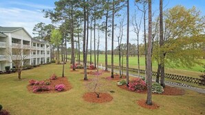 A hotel with a large building, a lawn with trees and shrubs, and a fence. - Cypress Point Retreat 202 (Myrtle Beach)