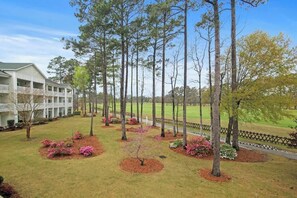 A hotel with a large building, a lawn with trees and shrubs, and a fence. - Cypress Point Retreat 202 (Myrtle Beach)
