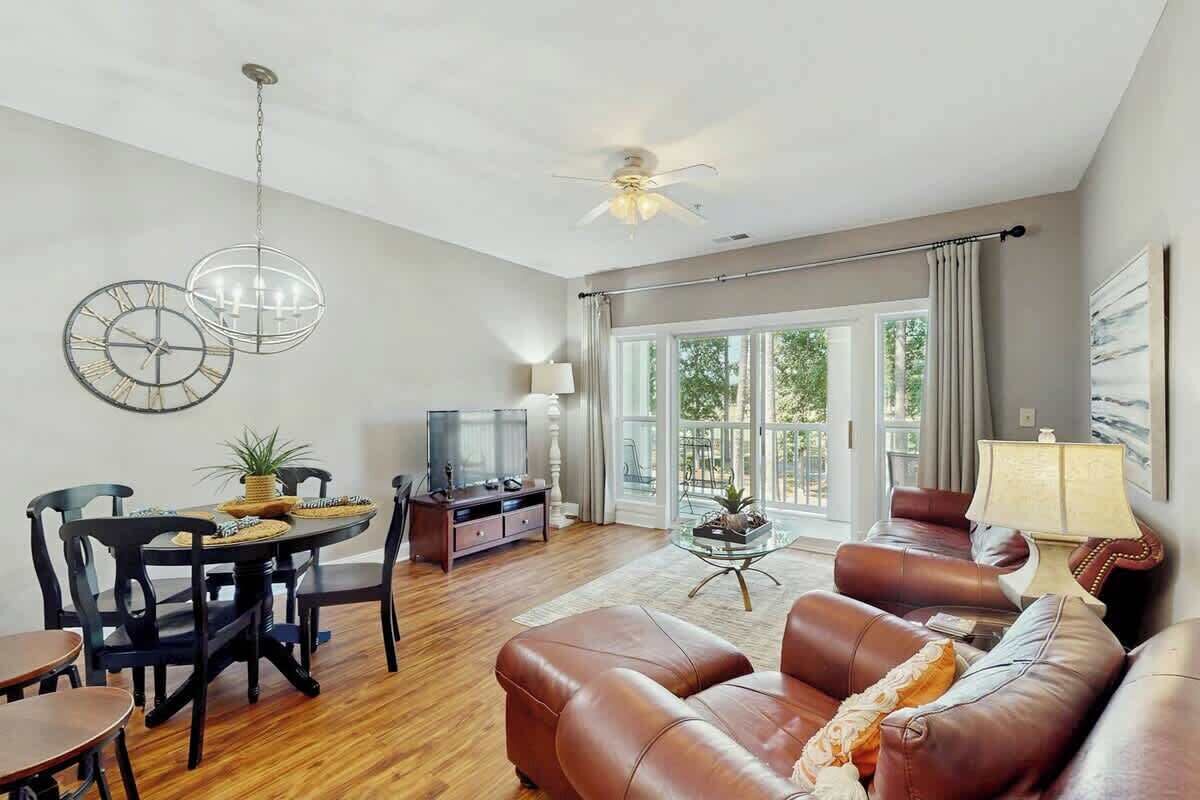 A living room with a brown leather sofa, a dining table with chairs, a TV, and a ceiling fan.