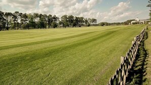 A well-maintained golf course with a wooden fence, trees, and a building in the background. - Cypress Point Retreat 202 (Myrtle Beach)