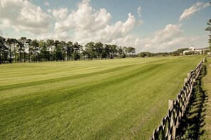 A well-maintained golf course with a wooden fence, trees, and a building in the background. - Cypress Point Retreat 202 (Myrtle Beach)